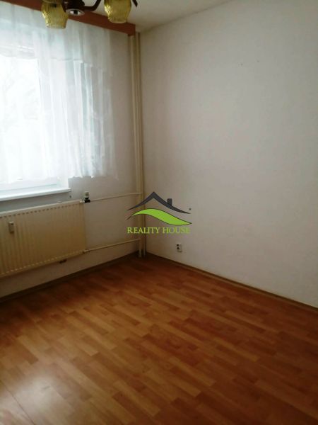 A room in a 3-room apartment with a wooden-patterned floor, curtain, and radiator.