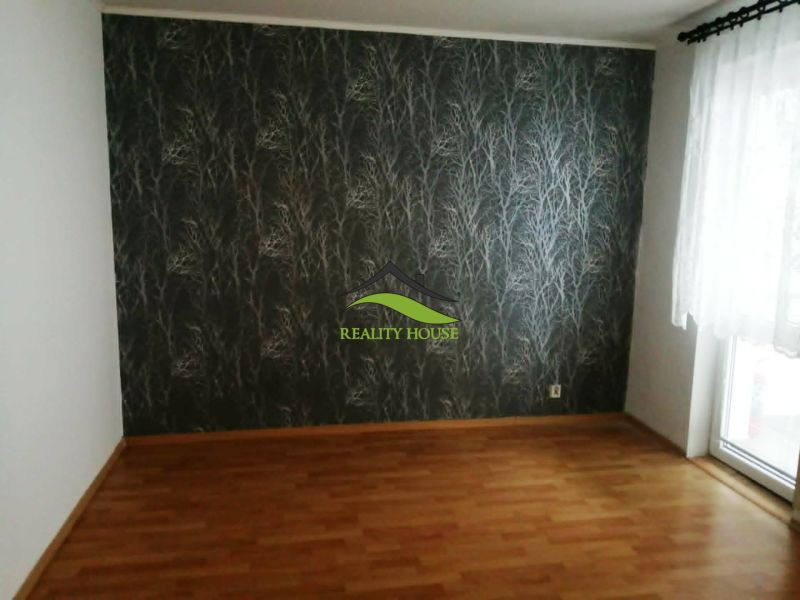 A room in a 3-room apartment with a wooden-patterned floor and patterned wallpaper.
