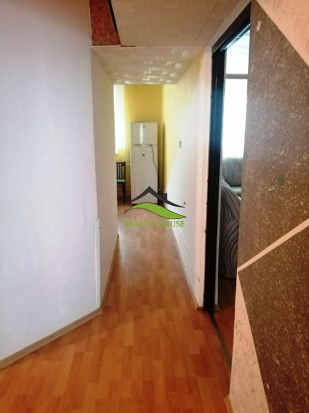 A hallway in a 3-room apartment with a wooden decor floor, leading to the refrigerator.