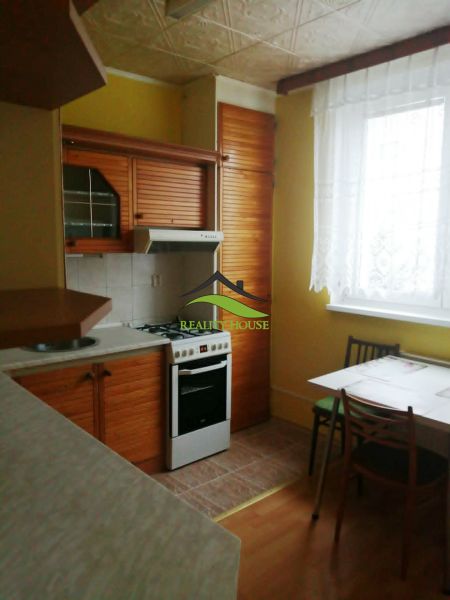 A kitchen in a 3-room apartment with a wooden decor floor, a dining table, and a stove.