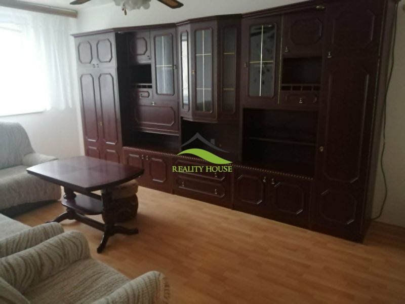 Living room with dark wooden furniture and wood-patterned flooring in a three-room apartment.