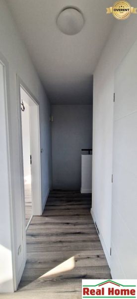 A hallway in a family house with white walls and a wooden-patterned floor.
