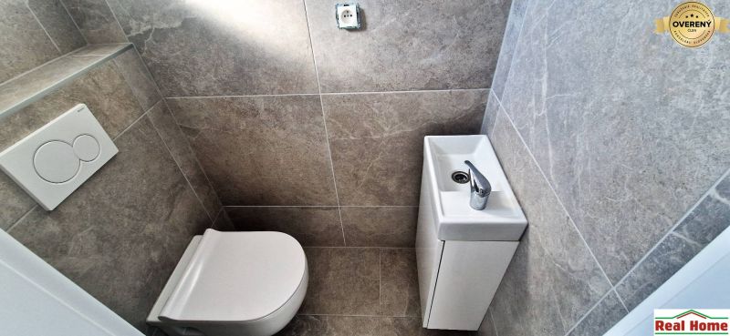 Toilet with a sink in a family house, gray wall tiles.