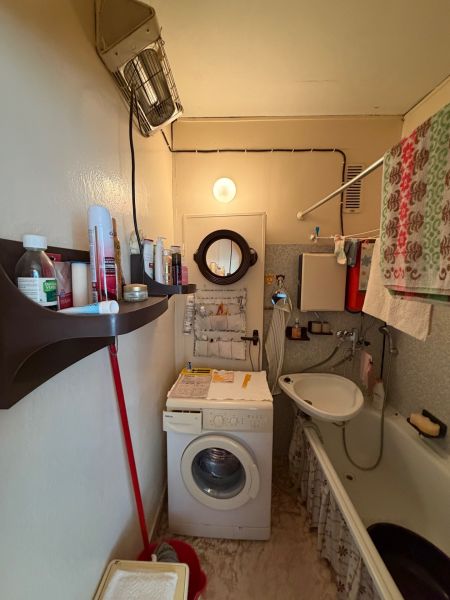 A bathroom in a 2-room apartment with a shower, sink, and washing machine.