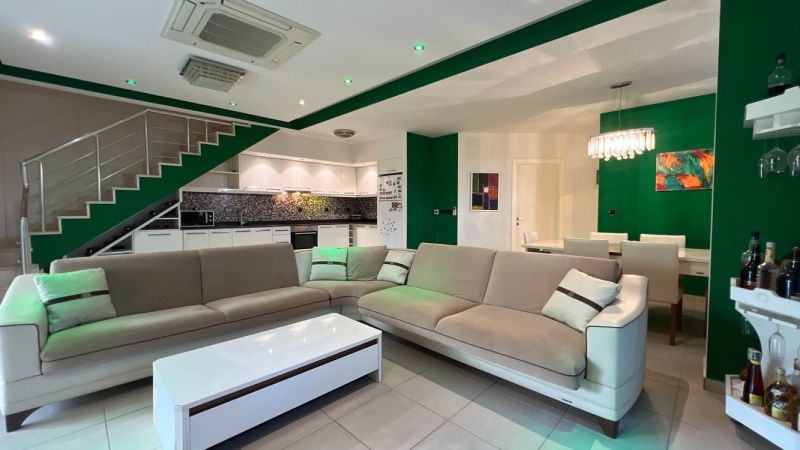 Living room with a sofa, dining table, kitchen, and green walls. Unique properties.