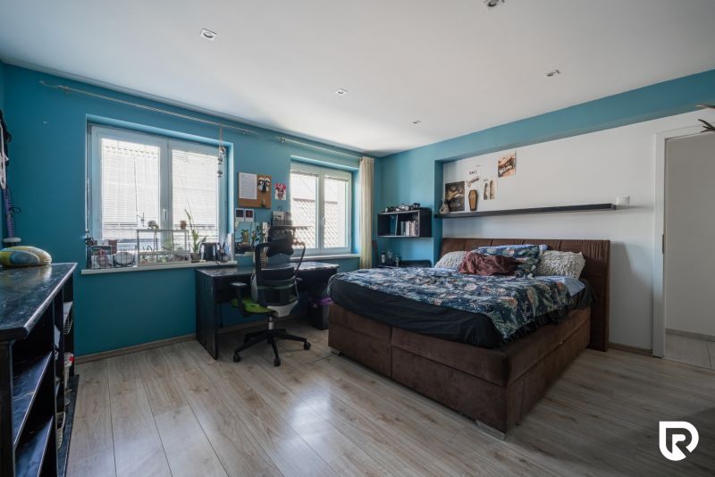 Bedroom in a family house, blue walls, bed, desk, and floor with wooden decor.