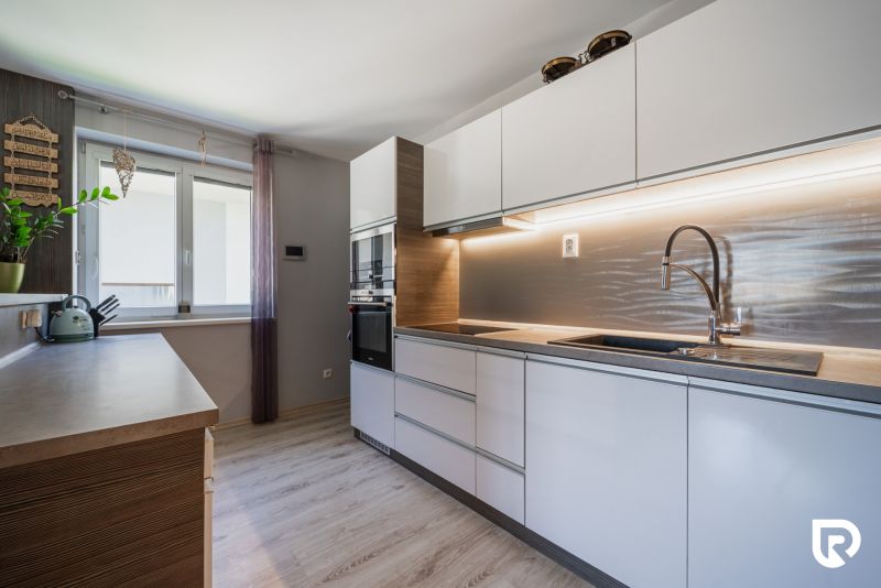 A kitchen in a family house with white cabinets, a wooden-patterned floor, and a window.