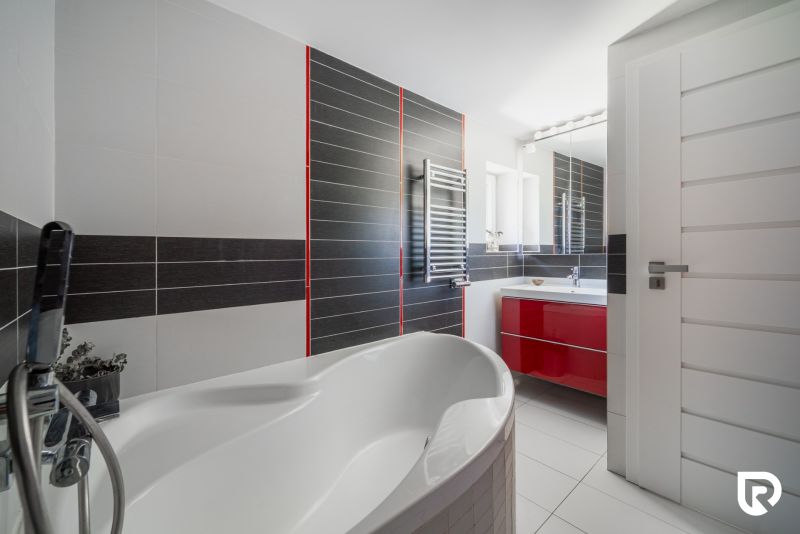 A bathroom in a family house with a bathtub, a red cabinet, and a silver radiator.