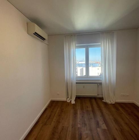 A room in a 3-room apartment with a wooden decor floor, air conditioning, and a window with a view.