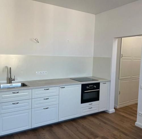 A kitchen in a 3-room apartment with white cabinets and a wood-patterned floor.