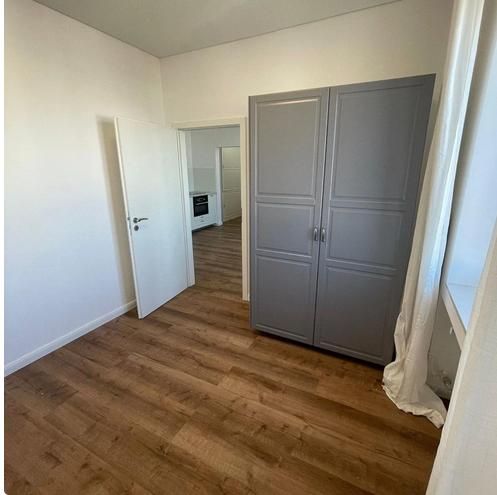 A room in a 3-room apartment with a wooden decor floor, a gray wardrobe, and a window.