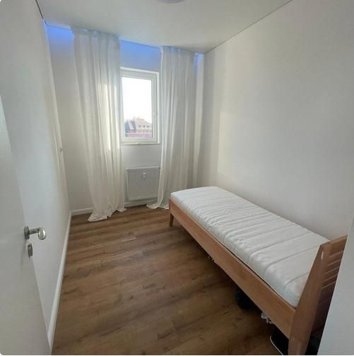 A narrow room with a bed and a wooden floor decor in a 3-room apartment.