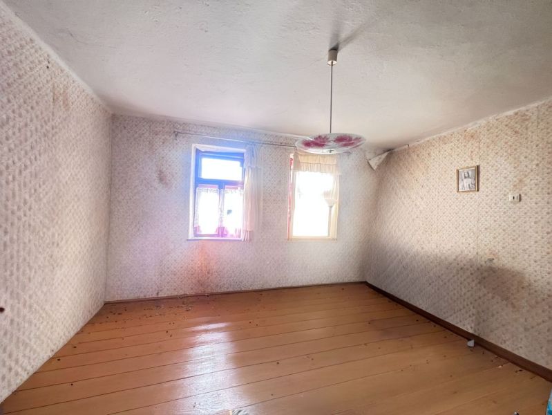 An empty room in a family house with a wooden decor floor and a floral chandelier.