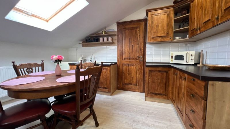 A kitchen in a villa with wooden cabinets, a dining table, and a floor with a wooden decor.