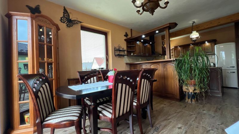 Dining area with chairs and a table, kitchen unit, floor with wood decor.