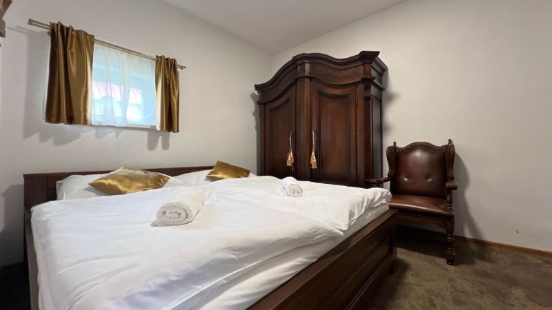 Bedroom in the villa with a cabinet, chair, bed, and golden pillows.