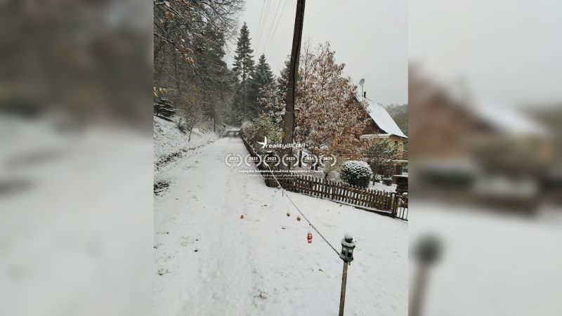 A snowy street in Horné Otrokovce with a family house and fencing.