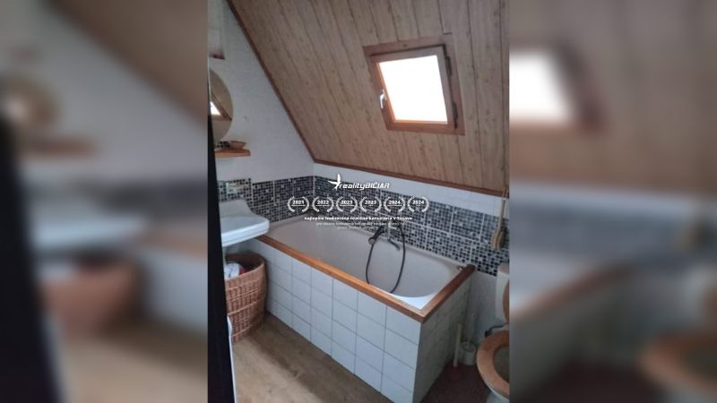 Bathroom with a bathtub and sloped ceiling, wooden decor, mosaic tiles, window.