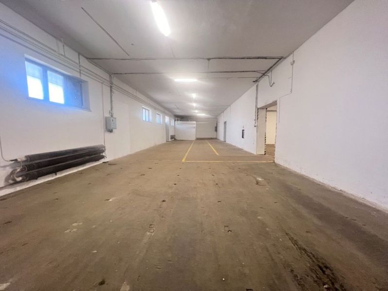 The interior of a warehouse with a concrete floor and white walls, fluorescent lighting.