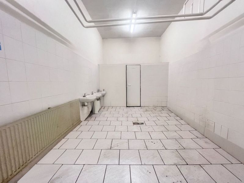 Interiors of warehouses and halls with white walls, two sinks, and tiled flooring.