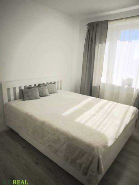 Bedroom with a bed and wooden decor flooring in a 2-room apartment, light curtains.