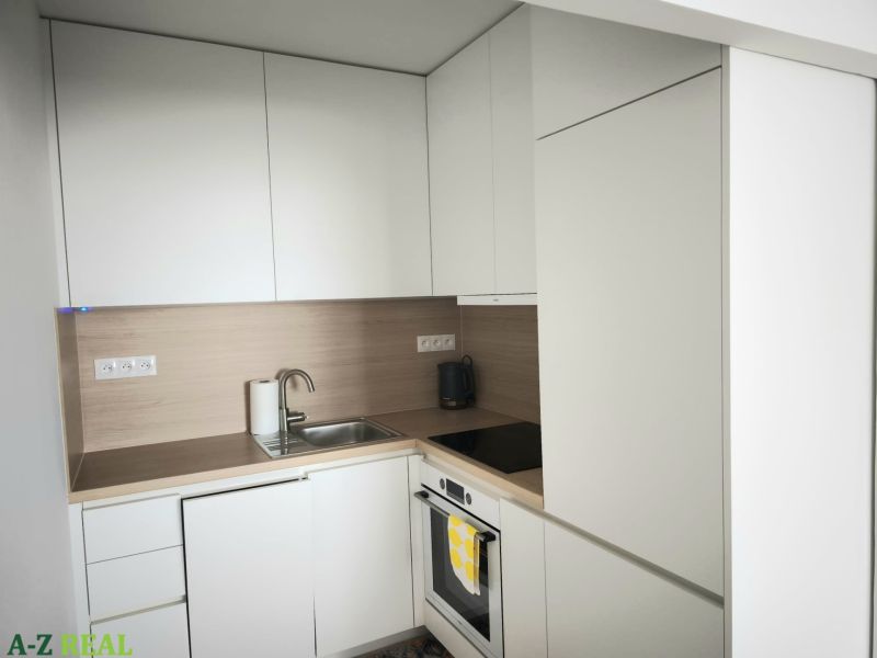 A kitchen with white cabinets and a stainless steel sink in a two-room apartment.