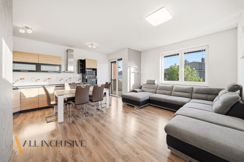 Living room with kitchen, large gray sofa, wooden decor flooring, 3-room apartment.