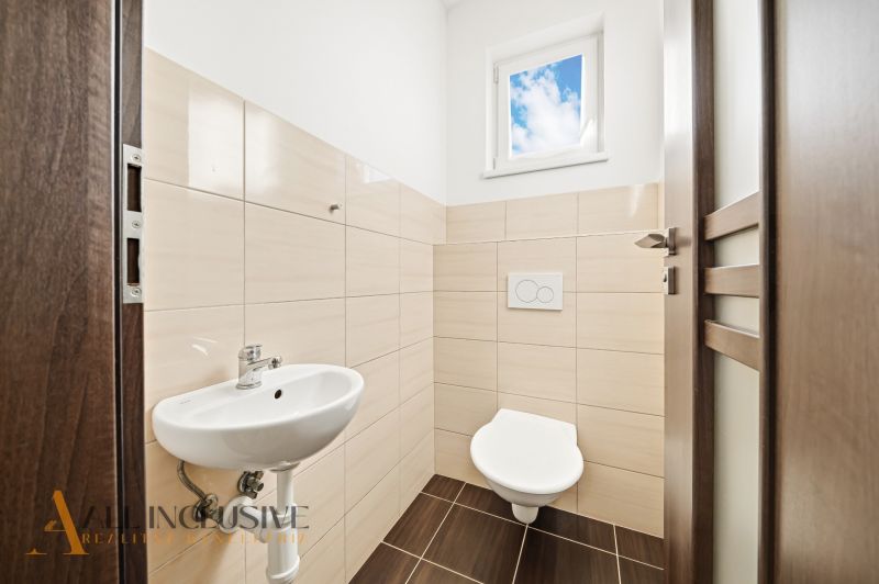 A bathroom in a 3-room apartment with a toilet, sink, and window.