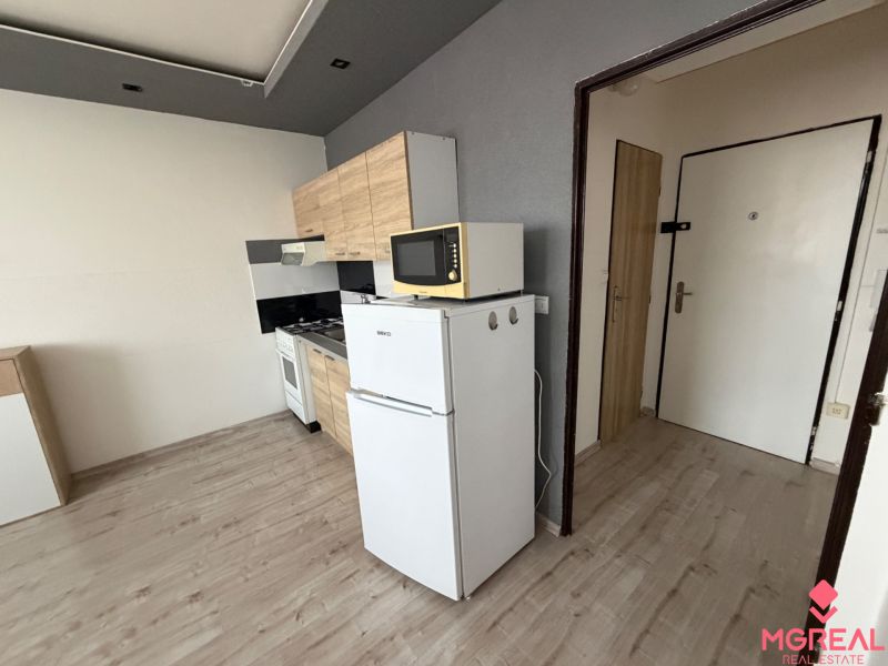 Kitchen in a studio apartment with a refrigerator and a wooden decor floor.