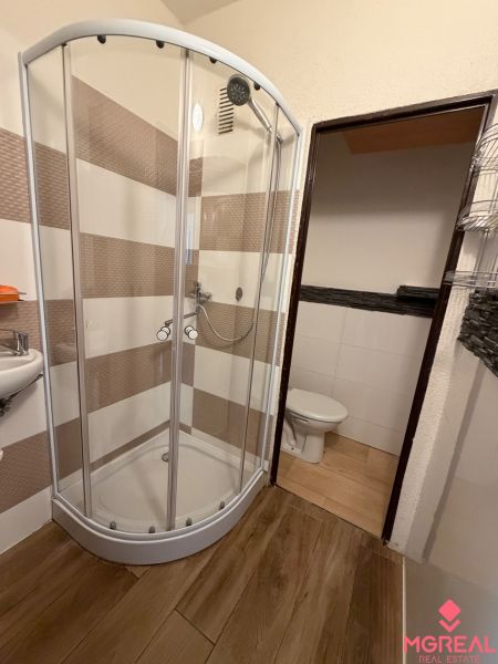 Shower corner and floor with wood decor in the bathroom of a studio apartment.