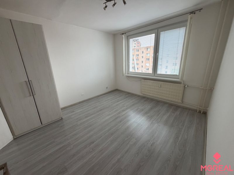 A room in a one-room apartment with a wooden decor floor and white walls.