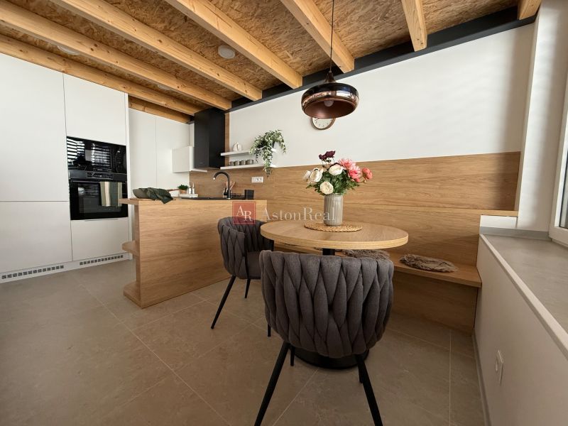 A kitchen in a family house with a wooden ceiling, a floor with a wooden decor, and stylish seating.