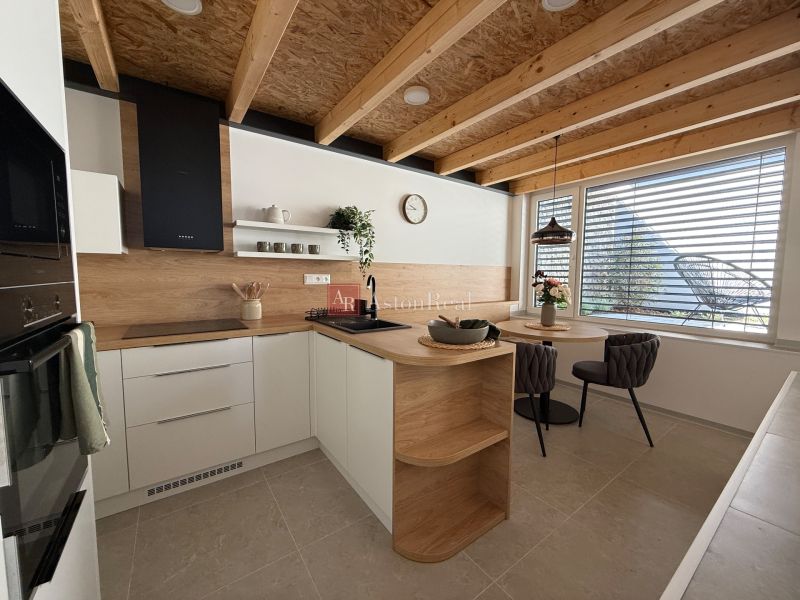 A kitchen in a family house with a wooden decor floor, wooden beams, and a dining table.