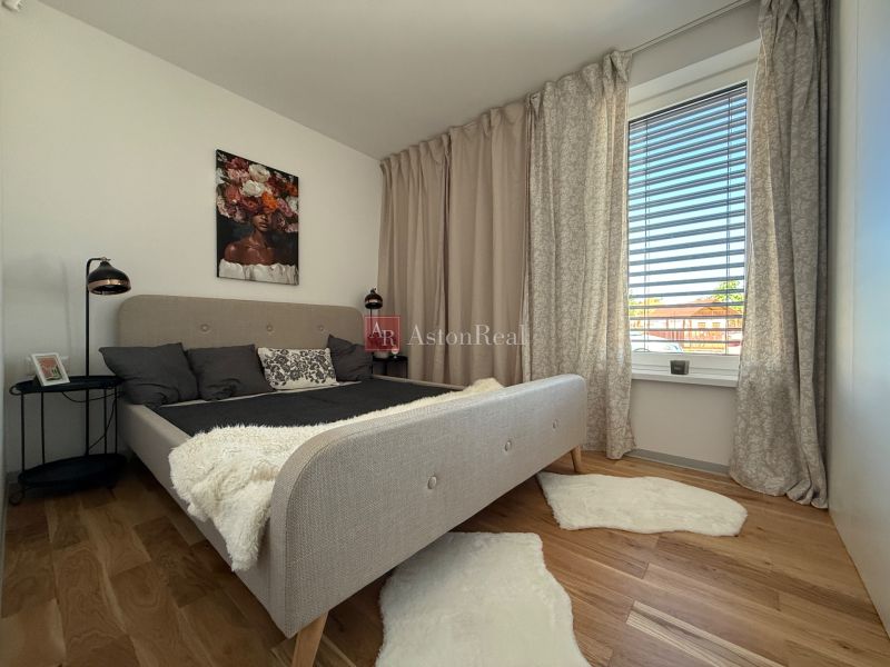 Bedroom with a bed, curtains, painting, and a wooden decor floor in a family house.