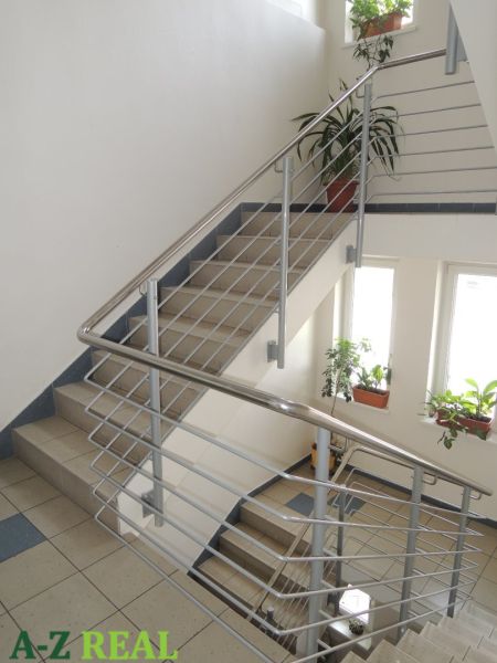 A staircase in the office with stainless steel railing, flowers, and large windows.