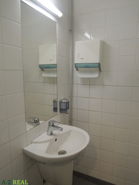A sink in offices with a soap dispenser and a mirror on the wall.