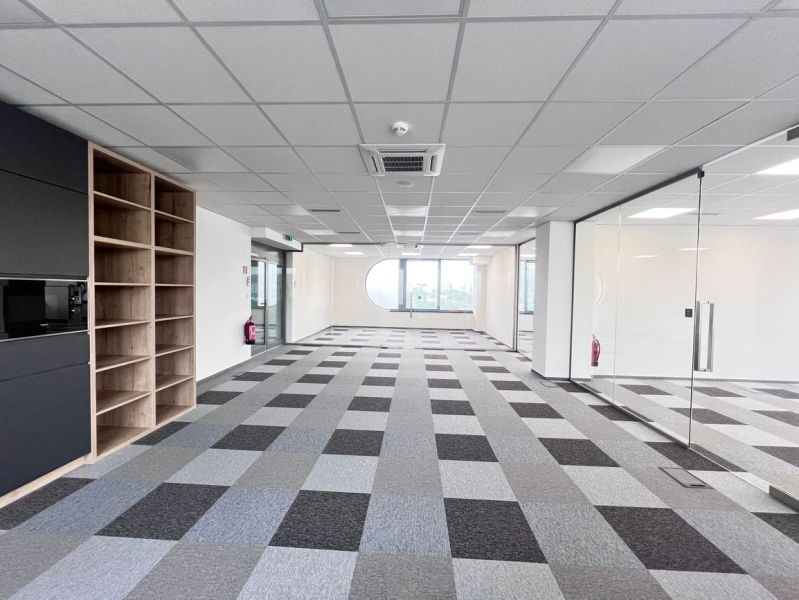 An office interior with carpet tiles, glass walls, and wooden decor.