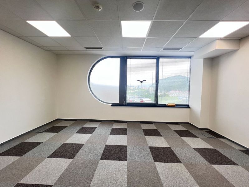Empty office with a window, gray patterned carpet, and a view of the mountains.