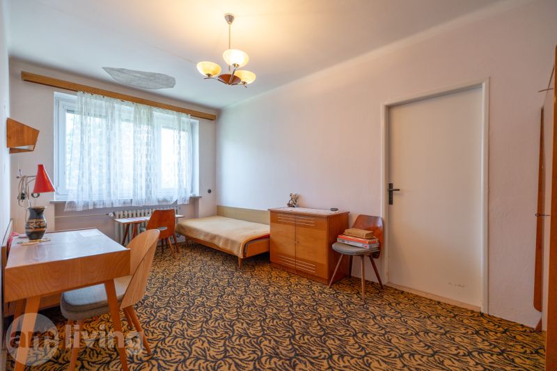 A room with a carpet, a desk, a bed, and cabinets in a three-room apartment.