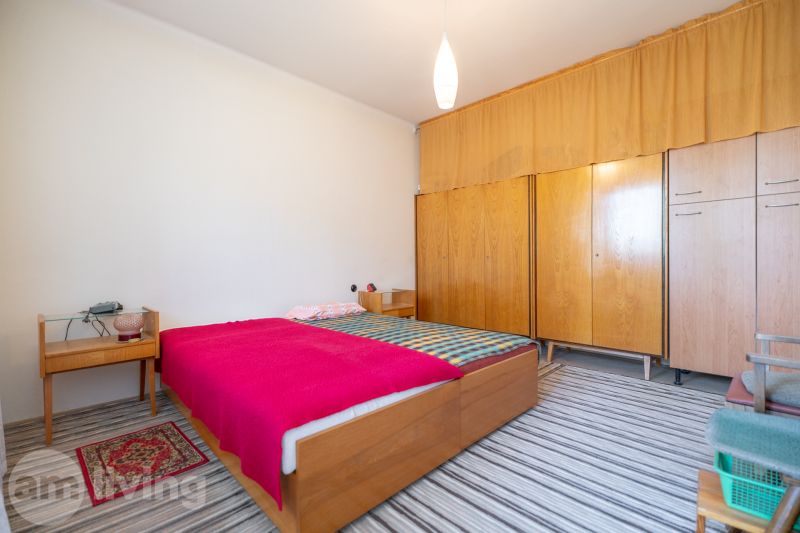 A bedroom in a three-room apartment with wooden furniture and a striped carpet.
