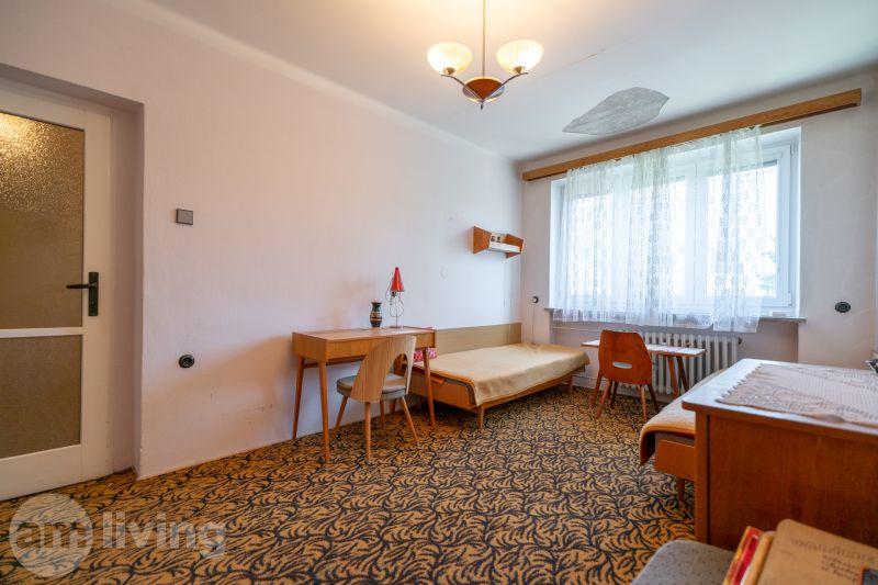A room in a 3-room apartment with a carpet, furniture, and a large window.