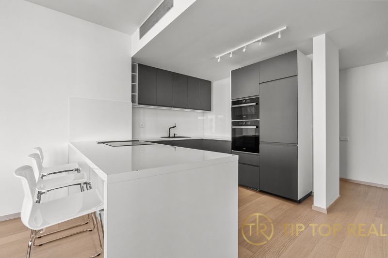 A minimalist kitchen in a 3-room apartment on Továrenská Street with modern equipment and bar stools.