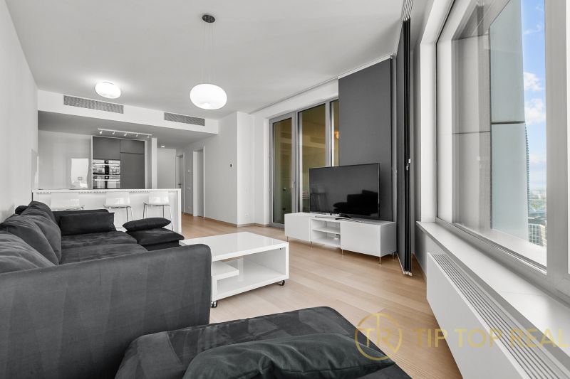 Living room with a dark sofa and a television, on Továrenská street, part of a 3-room apartment.