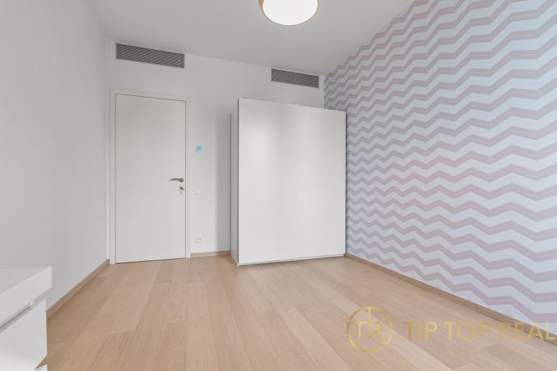 A bright room with parquet floors, a white wardrobe, and patterned wallpaper on Továrenská Street.