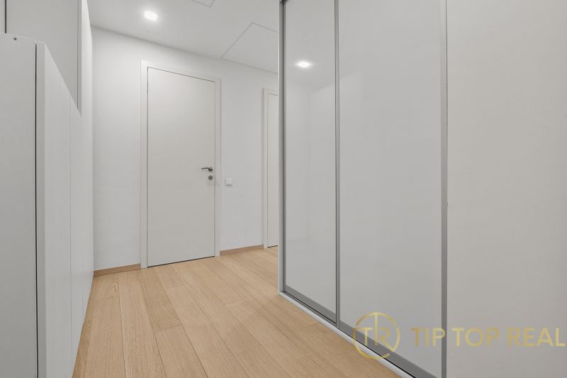 A hallway with a wooden floor and a white built-in wardrobe, located on Továrenská Street.