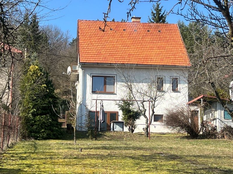 A family house in Kráľová, Banská Bystrica, with a red roof surrounded by greenery and trees.
