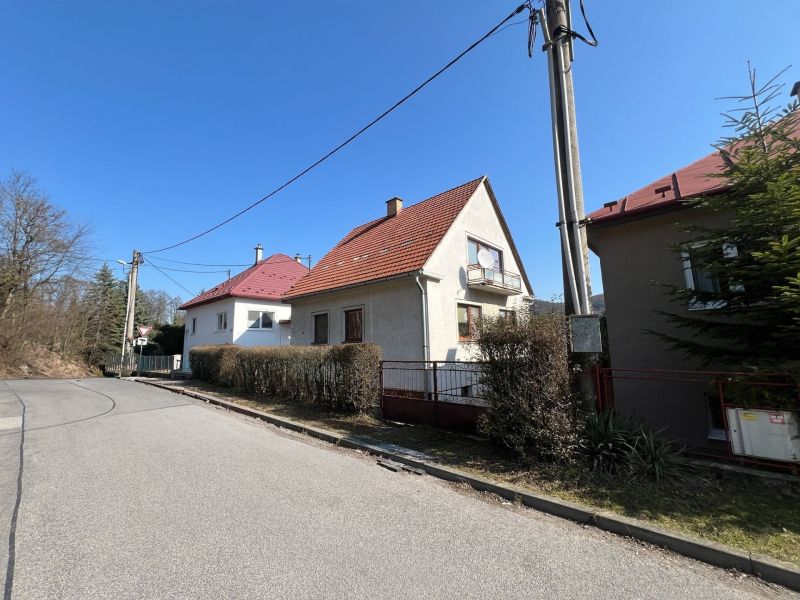 Family house in Podháj, Kráľová, Banská Bystrica. Narrow sidewalk, bushes, electric pole.
