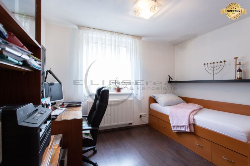 A room in a family house with a bed, a desk, and a wooden-patterned floor.