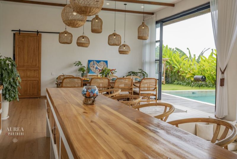 Interior of a villa with wood-patterned flooring, wicker light fixtures, and a pool.