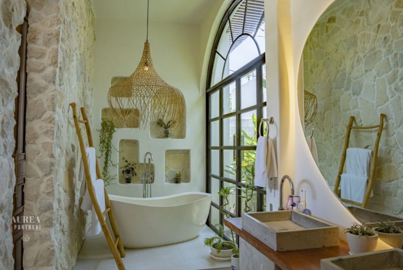 A bathroom in a villa with a bathtub, stone walls, and a large arched window.